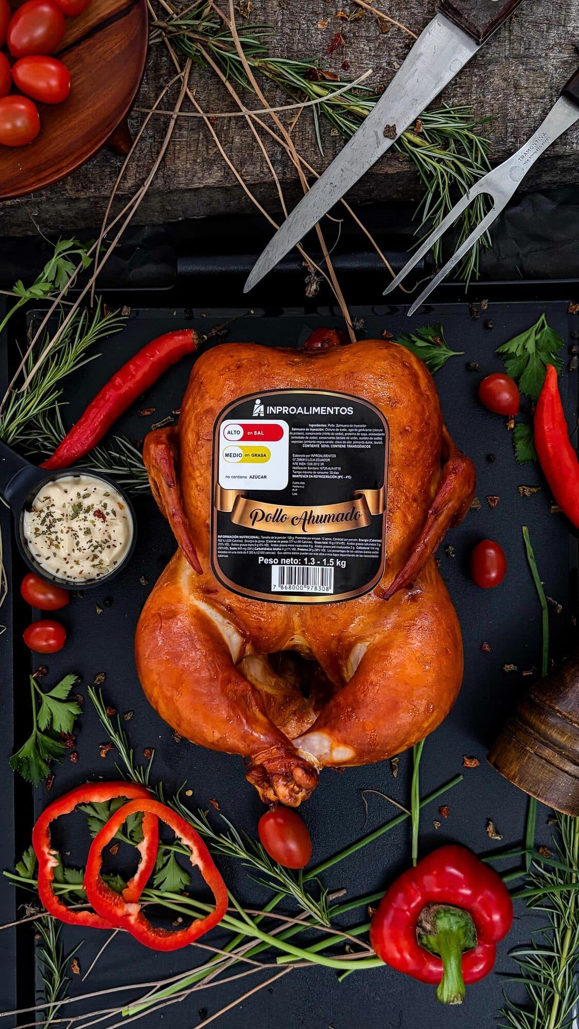 Pollo ahumado entero sobre bandeja negra con romero y ajíes